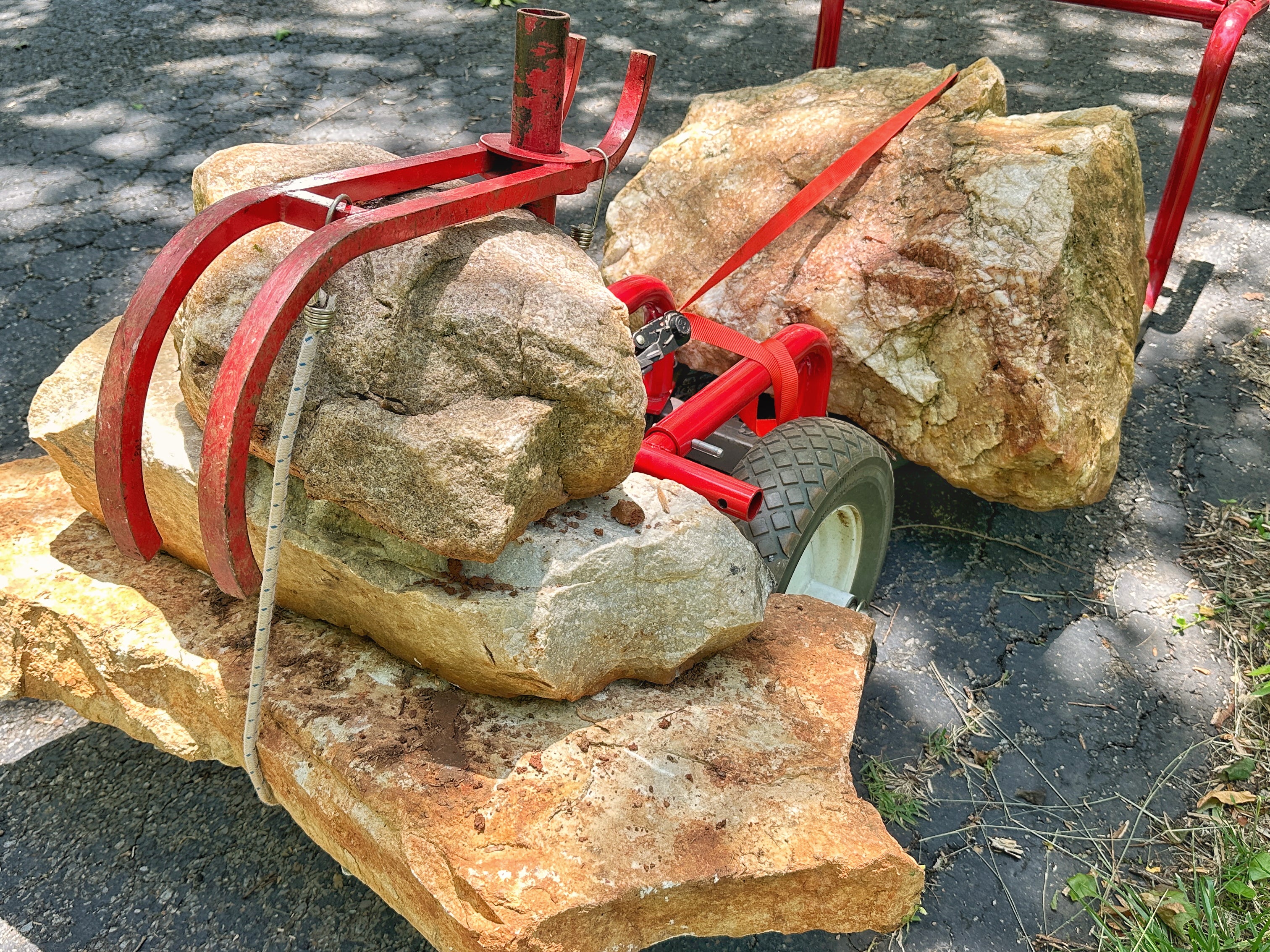 Red mechanical device lifting large stones on a road