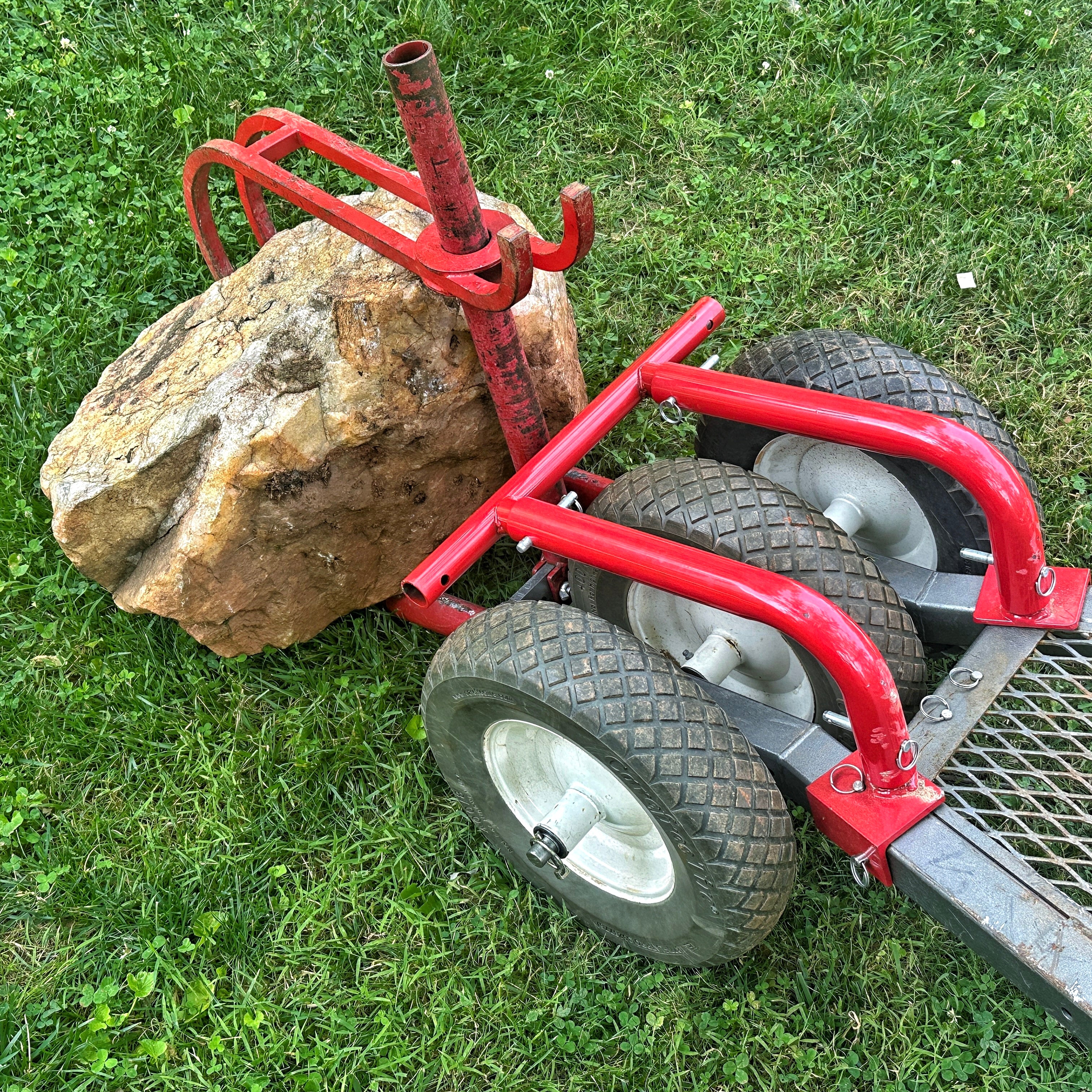 Red manual dolly with wheels pushing a large rock on grass