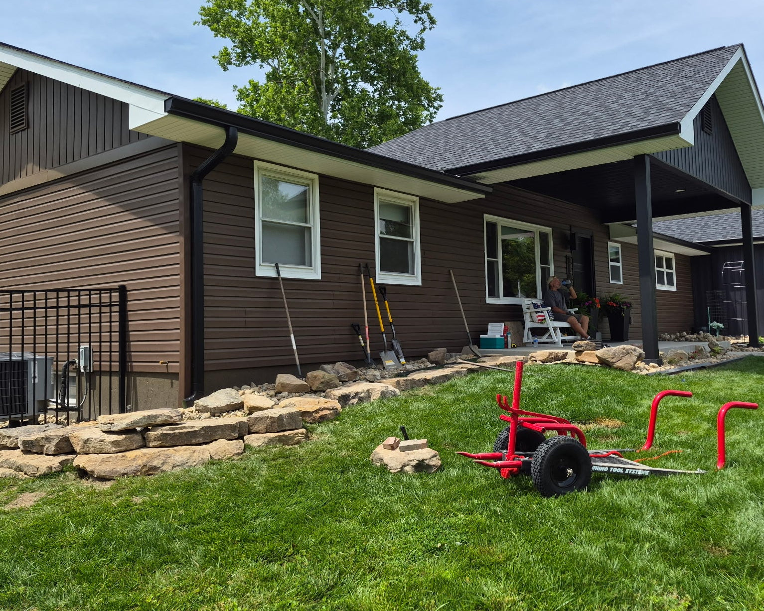 a brown house with a stone retaining wall and a rock moving cart in the front yard