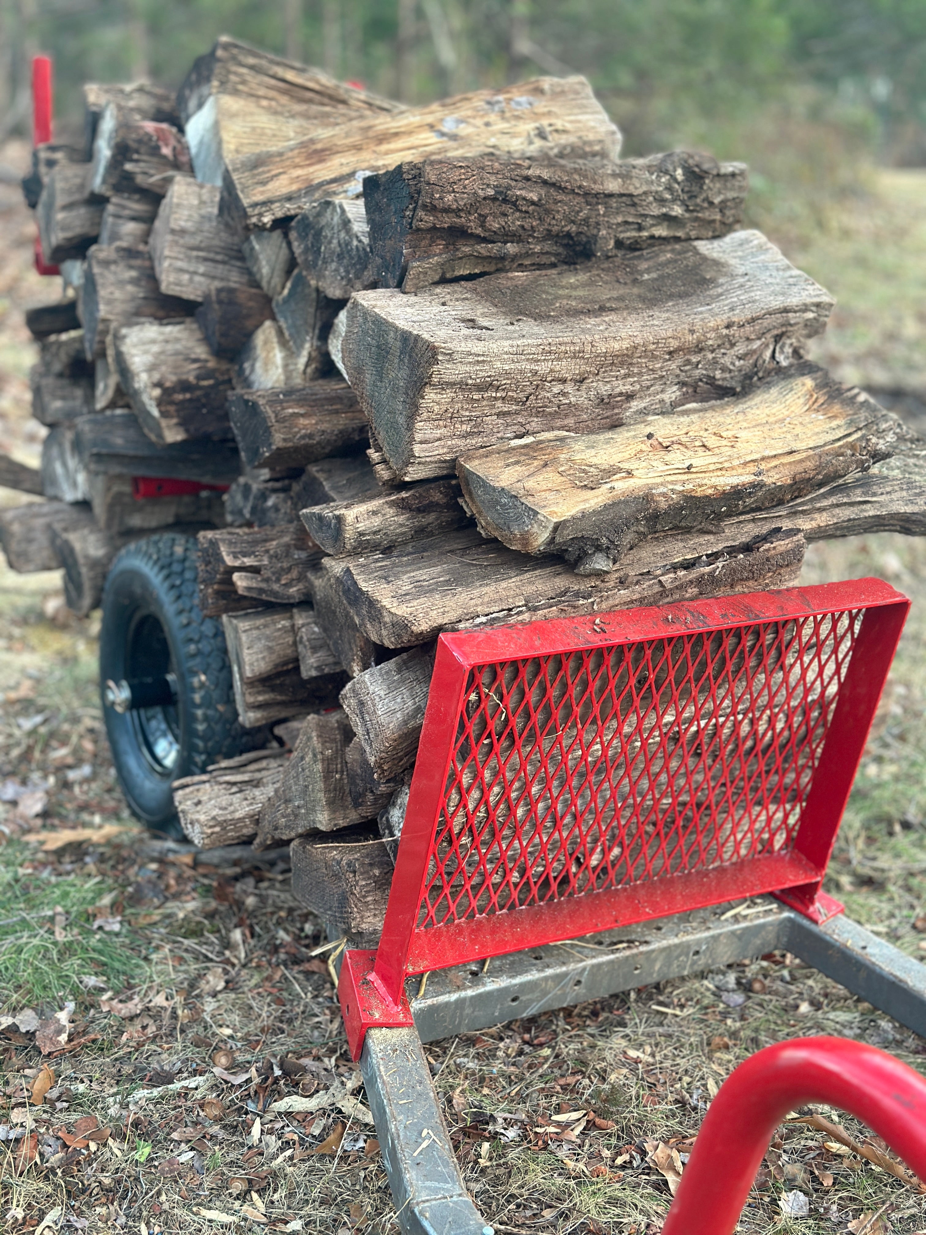 Stack of firewood on a cart with a red metal grate in an outdoor setting