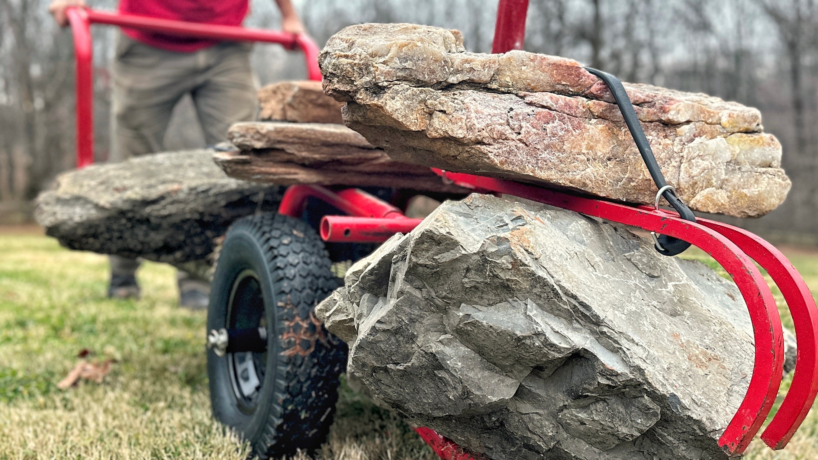 Rhino rock hauler loaded with stone and being pushed by a man in a red shirt